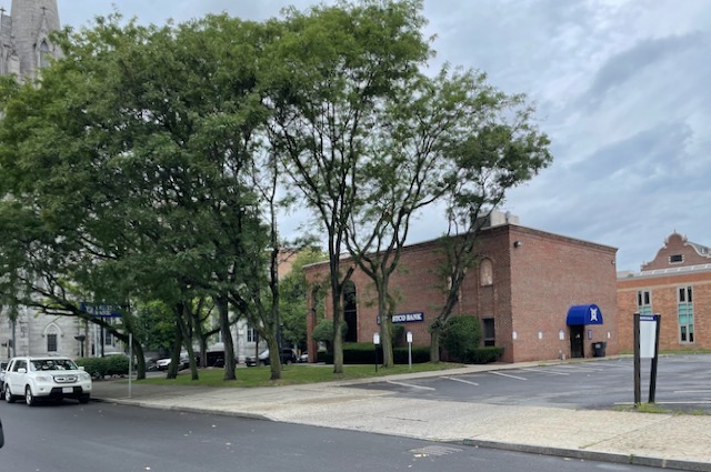 The spire of Christ Church United Methodist is at the left, the area immediately behind the sign at right is where Union St (alley) was. The black-topped parking lot was the site of the church. Out of site at the right are the municipal buildings and Police Station (corner State and Sixth.)